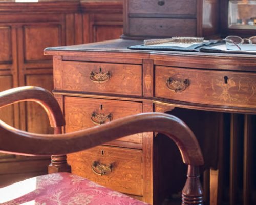 Fine antique pedestal writing desk and chair. Studying history and period drama. Ornate regency table with reading and author materials. Magnifying glass, glasses or spectacles, and fountain pen.