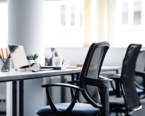 Modern gadgets in interior of coworking office during COVID-19 epidemic. Chairs and desk for support workers, laptops and headphones, cups and stationery in daylight on window background, free space
