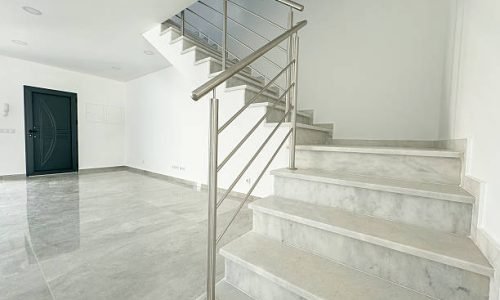 Spacious home entrance featuring polished gray flooring, a dark door, and a contemporary staircase.
